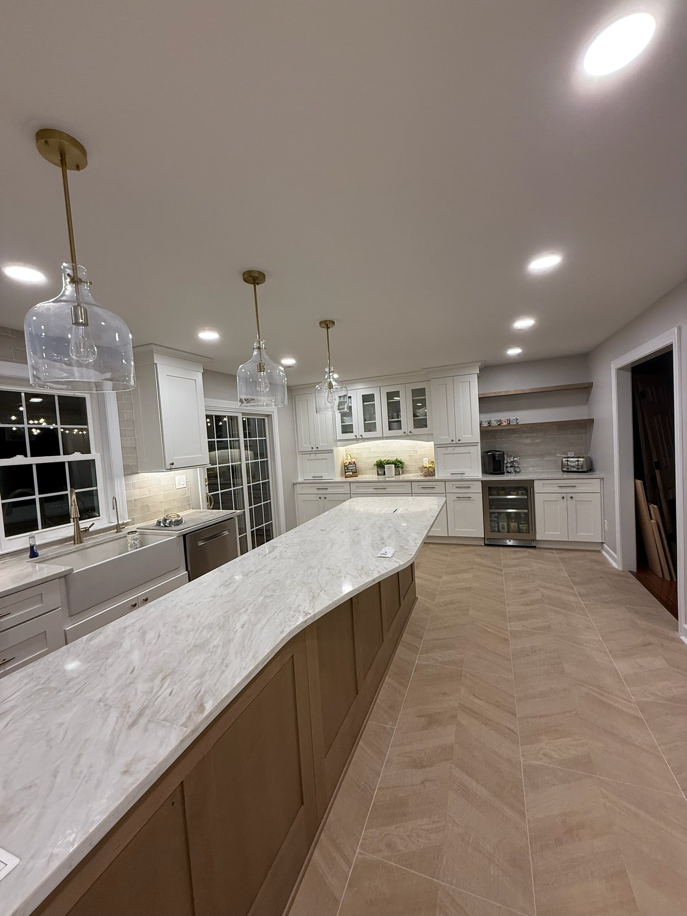 After the remodel: white cabinets, a longer island, tile floor, and pendant lights
